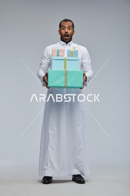 رجل سعودي يرتدي الثوب التقليدي يحمل صناديق هدايا مندهش