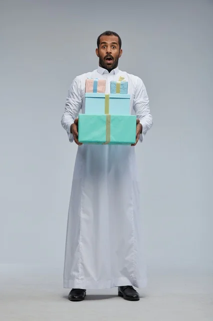 رجل سعودي يرتدي الثوب التقليدي يحمل صناديق هدايا مندهش