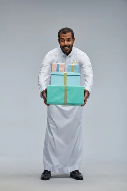 رجل سعودي بالزي التقليدي يحمل صناديق هدايا ملونة