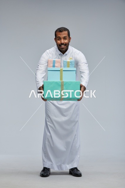 رجل سعودي بالزي التقليدي يحمل صناديق هدايا ملونة