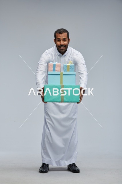 رجل سعودي بالزي التقليدي يحمل صناديق هدايا ملونة