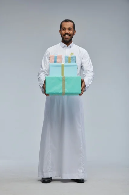رجل سعودي بالزي التقليدي يحمل مجموعة صناديق هدايا