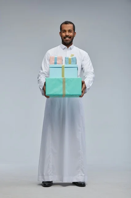 رجل سعودي بالزي التقليدي يحمل صناديق هدايا ملونة