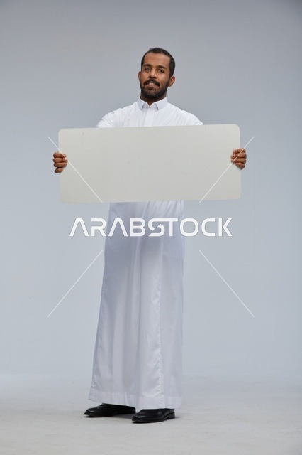 رجل سعودي مبتسم يحمل لوحة بيضاء فارغة في استوديو