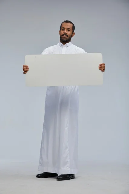 رجل سعودي مبتسم يحمل لوحة بيضاء فارغة في استوديو