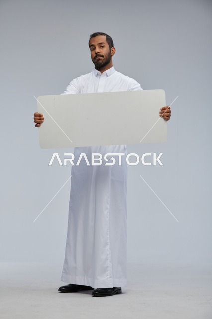 رجل سعودي بالثوب يحمل لوحة بيضاء فارغة للإعلان