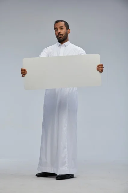 رجل سعودي بالثوب يحمل لوحة بيضاء فارغة للإعلانات