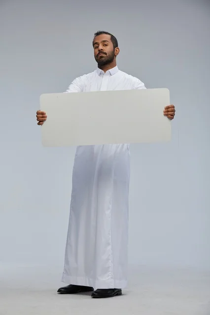 رجل سعودي بالزي التقليدي يحمل لوحة بيضاء فارغة للإعلان