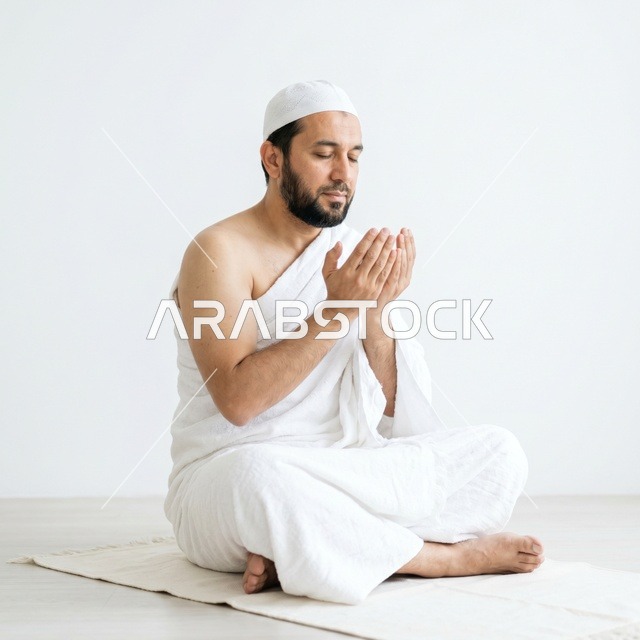 رجل مسلم بملابس الإحرام يؤدي الدعاء على سجادة الصلاة
