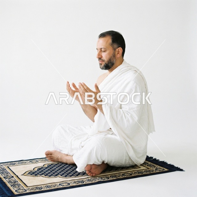 رجل مسلم بملابس الإحرام يدعو على سجادة الصلاة