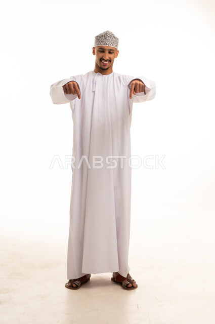 رجل عماني بالزي التقليدي والدشداشة البيضاء يشير للأسفل