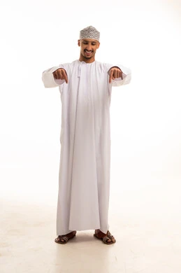 رجل عماني بالزي التقليدي والدشداشة البيضاء يشير للأسفل
