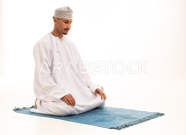 رجل عماني بالزي التقليدي يصلي على السجادة