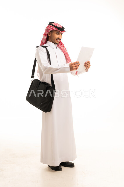 رجل سعودي بالثوب يقرأ مستنداً على خلفية بيضاء