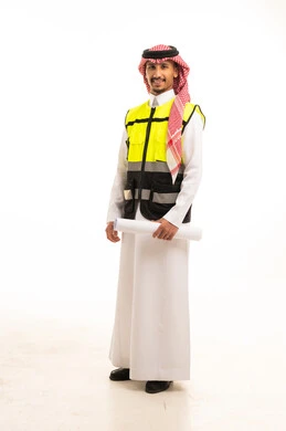 مهندس سعودي يرتدي سترة السلامة ويحمل مخططاً هندسياً