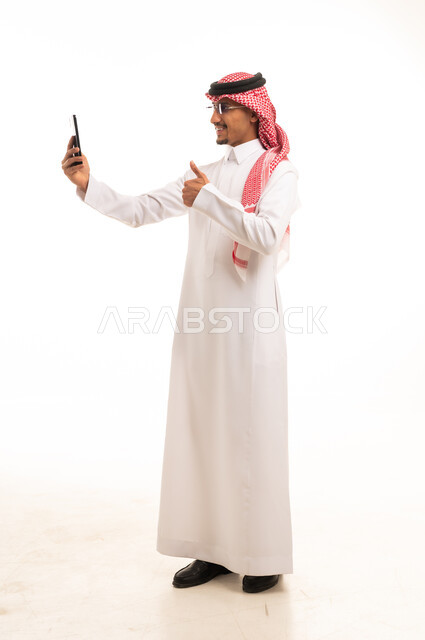 رجل سعودي بالثوب التقليدي يستخدم الهاتف الذكي