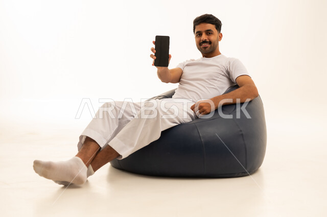 رجل سعودي يحمل هاتفا ذكيا على مقعد محشو
