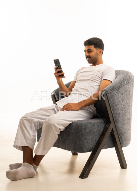 رجل سعودي يجلس على كرسي يستخدم الهاتف الذكي