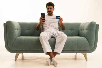رجل سعودي يستخدم بطاقة الائتمان والجوال على الأريكة