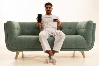 رجل سعودي يحمل هاتف ذكي وبطاقة بنكية على أريكة