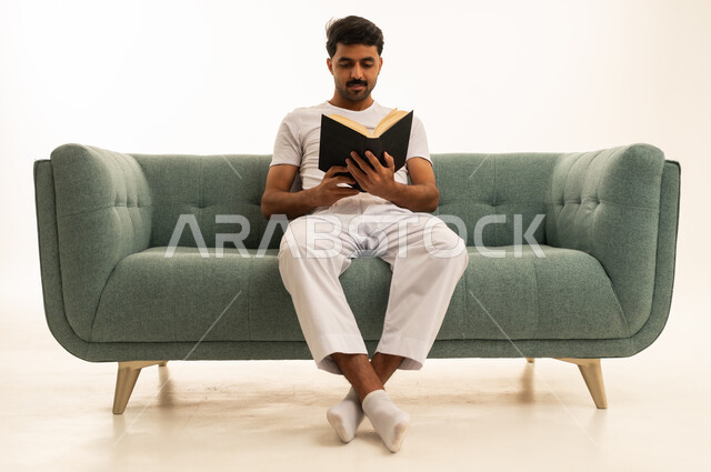 رجل سعودي يقرأ كتاباً على أريكة خضراء