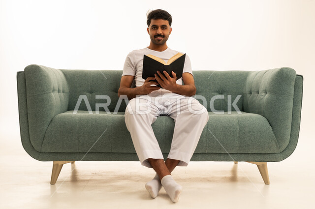 رجل سعودي يقرأ كتاباً أسود على أريكة في الاستوديو