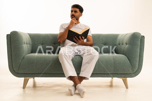 رجل سعودي يقرأ كتاباً على أريكة خضراء
