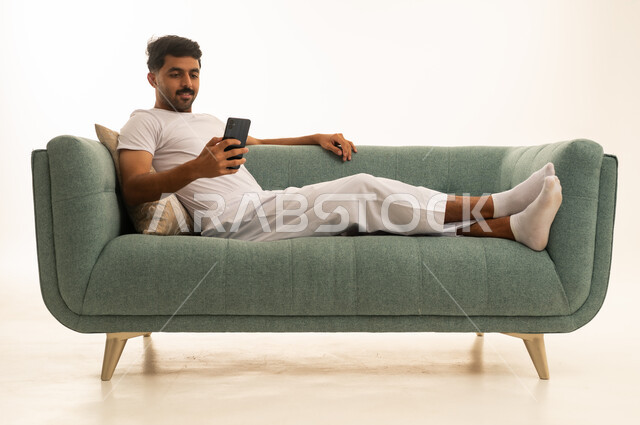 رجل سعودي يسترخي على أريكة خضراء يستخدم الجوال