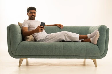 رجل سعودي على أريكة خضراء يستخدم الجوال
