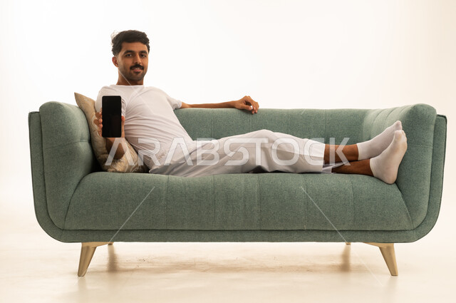 Saudi Man Holding Smartphone on Green Sofa Mockup