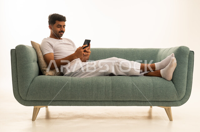 رجل سعودي يستخدم الهاتف الذكي على الأريكة