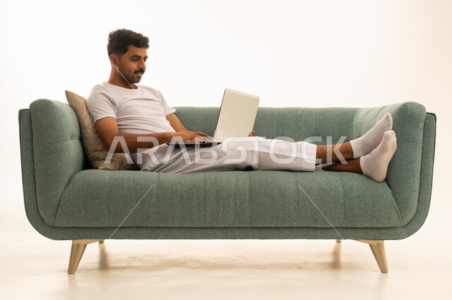 رجل سعودي يستخدم اللابتوب على أريكة خضراء في الاستوديو