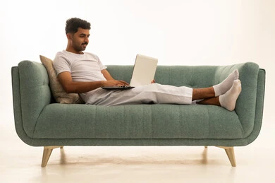 رجل سعودي يستخدم اللابتوب على أريكة خضراء في الاستوديو