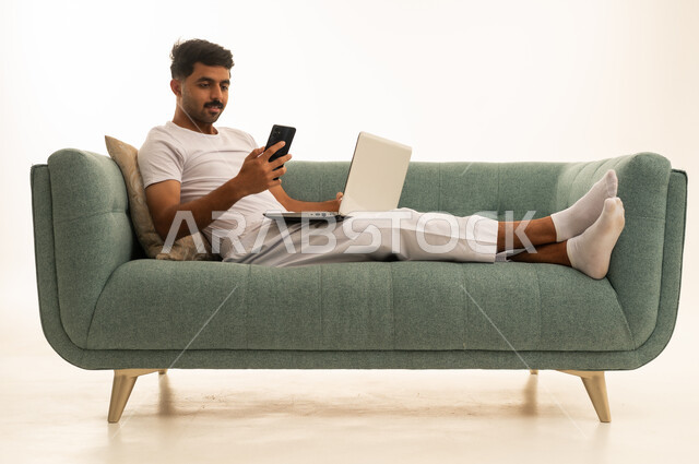 شاب سعودي يستخدم الحاسوب والجوال على أريكة