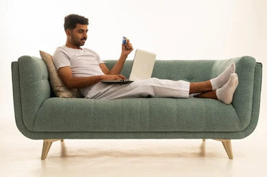 رجل عربي مع حاسوب وبطاقة ائتمان على أريكة