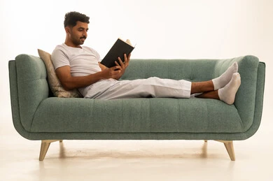 رجل سعودي يقرأ كتاباً على أريكة خضراء بخلفية بيضاء