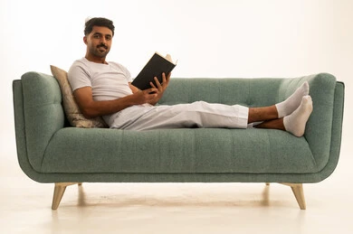 رجل سعودي يقرأ كتاباً على أريكة حديثة في خلفية بيضاء