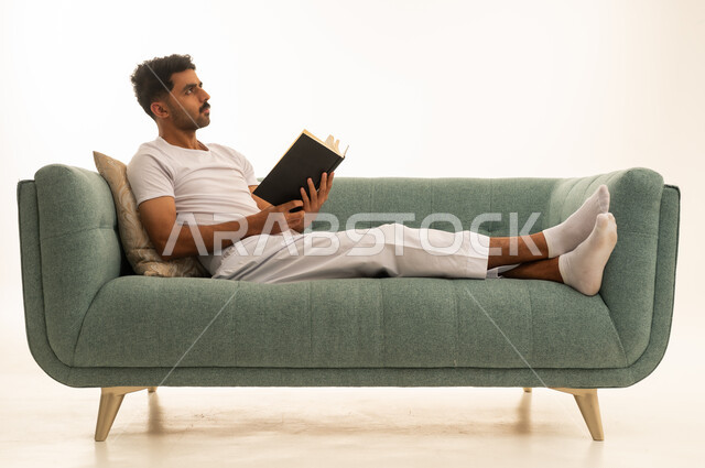 Saudi Man Reading Book on Green Sofa in Loungewear