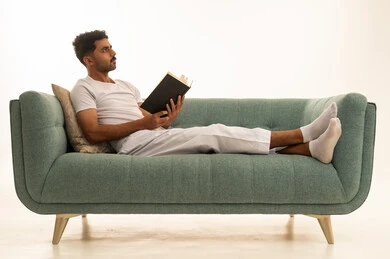 رجل سعودي يقرأ كتاباً على أريكة خضراء بملابس منزلية