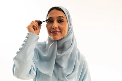 امرأة عربية بالحجاب تضع المسكارا بخلفية بيضاء امرأة عربية بالحجاب تضع المسكارا بخلفية بيضاء