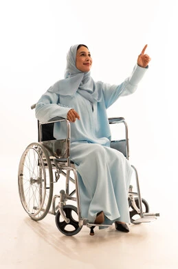 امرأة عربية على كرسي متحرك بعباءة زرقاء تشير للأعلى