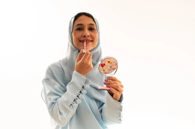 امرأة إماراتية تضع المكياج مع مرآة على خلفية بيضاء