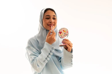 امرأة عربية ترتدي الحجاب تضع ملمع الشفاه بخلفية بيضاء