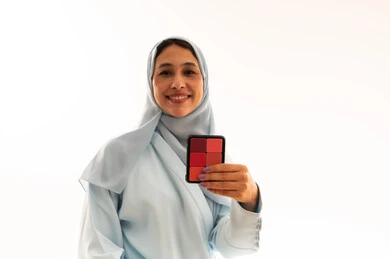 امرأة عربية بالحجاب تمسك لوحة مكياج أمام خلفية بيضاء