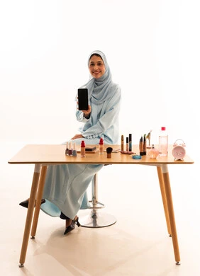 Emirati Woman Holding Smartphone with Makeup on Table