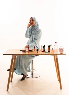 امرأة عربية بالحجاب مع مستحضرات تجميل على الطاولة