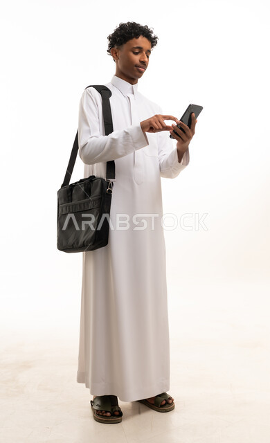 شاب سعودي بالثوب الأبيض يستخدم الهاتف الذكي في استوديو