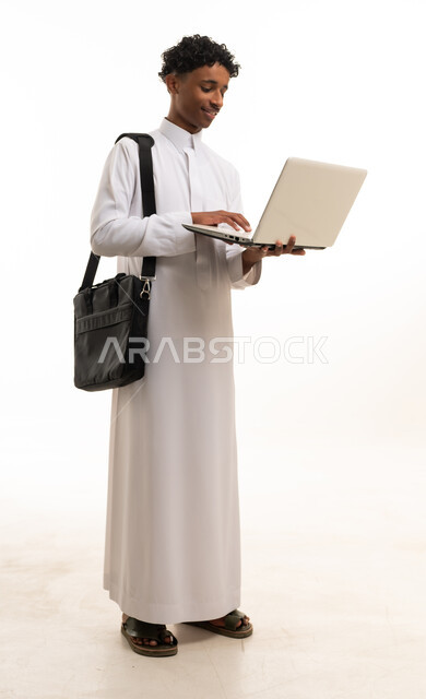 شاب سعودي بالثوب الأبيض يحمل كمبيوتر محمول بخلفية بيضاء