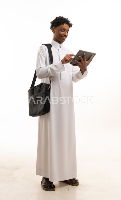 شاب سعودي بالثوب يستخدم جهاز لوحي مع حقيبة محمول
