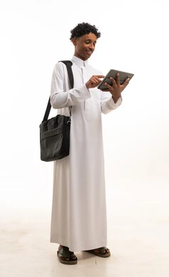 شاب سعودي بالثوب يستخدم جهاز لوحي مع حقيبة محمول